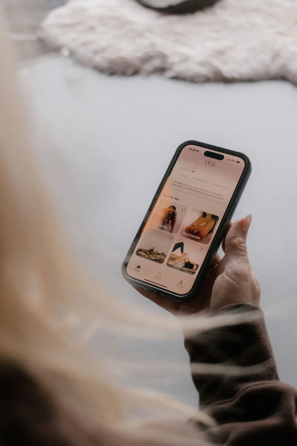 A hand holding a phone open to the Déjà Well Today screen, with meditation, breathwork, food and self care cards