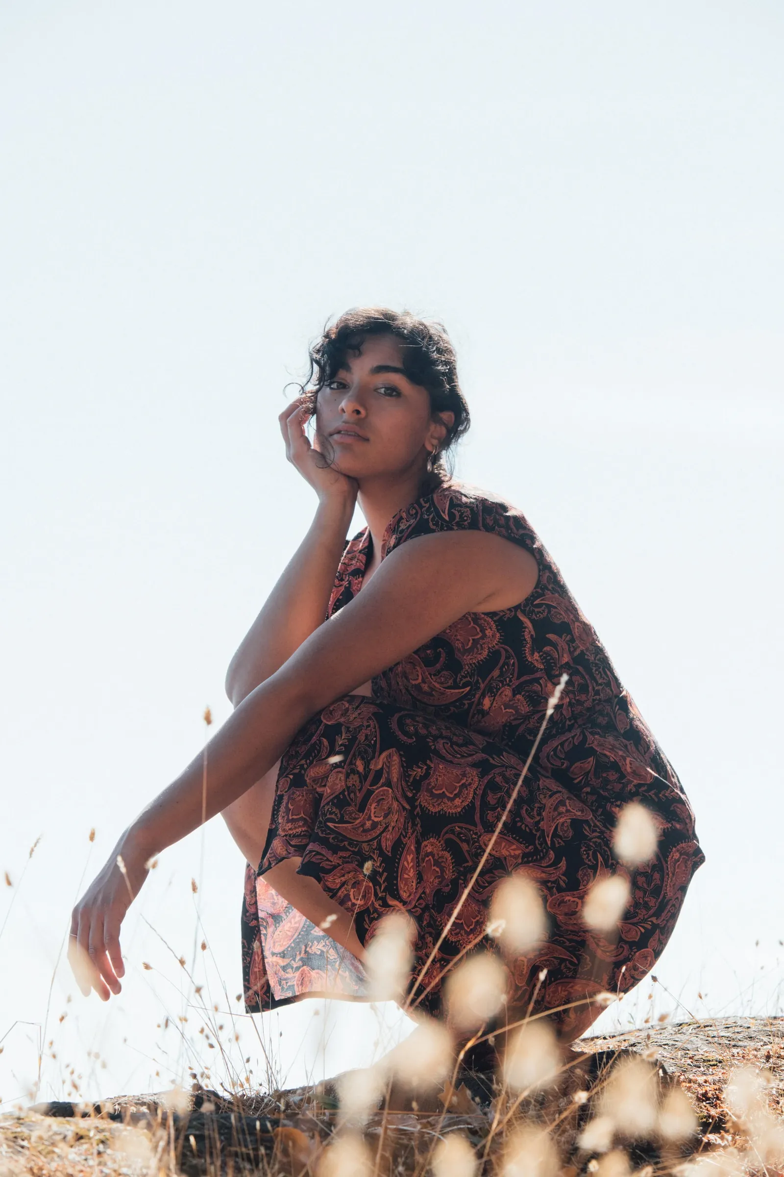 A woman sitting in long grass by the water at golden hour